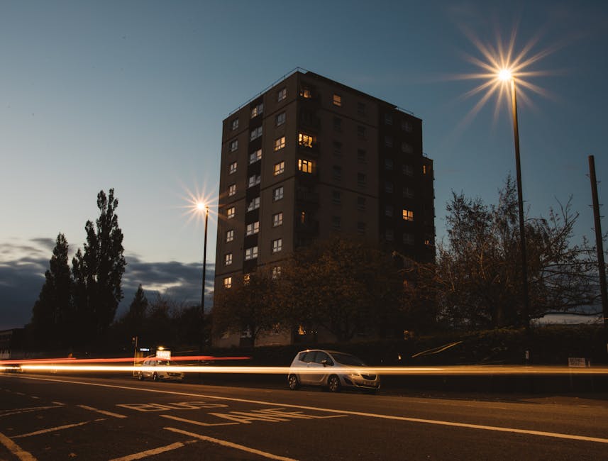 A residential area along King Georges Road featuring modern multi-story apartment buildings constructed with light-colored bricks and large windows. The scene includes a sloped sidewalk with a parked 